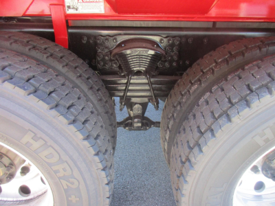 Dual rear tires and suspension view showing air ride or coil spring mechanism and differential housing under a red dump truck.