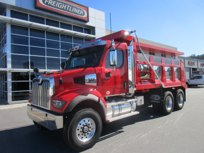 Western Star 47X dump truck in red parked outside dealership with chrome exhaust and large front grille, three axles and dump bed visible.