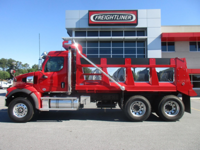 Western Star 47X dump truck in red parked in front of Freightliner dealership building. Side view shows long dump bed, chrome exhaust, dual rear axles, and chrome fuel tanks.