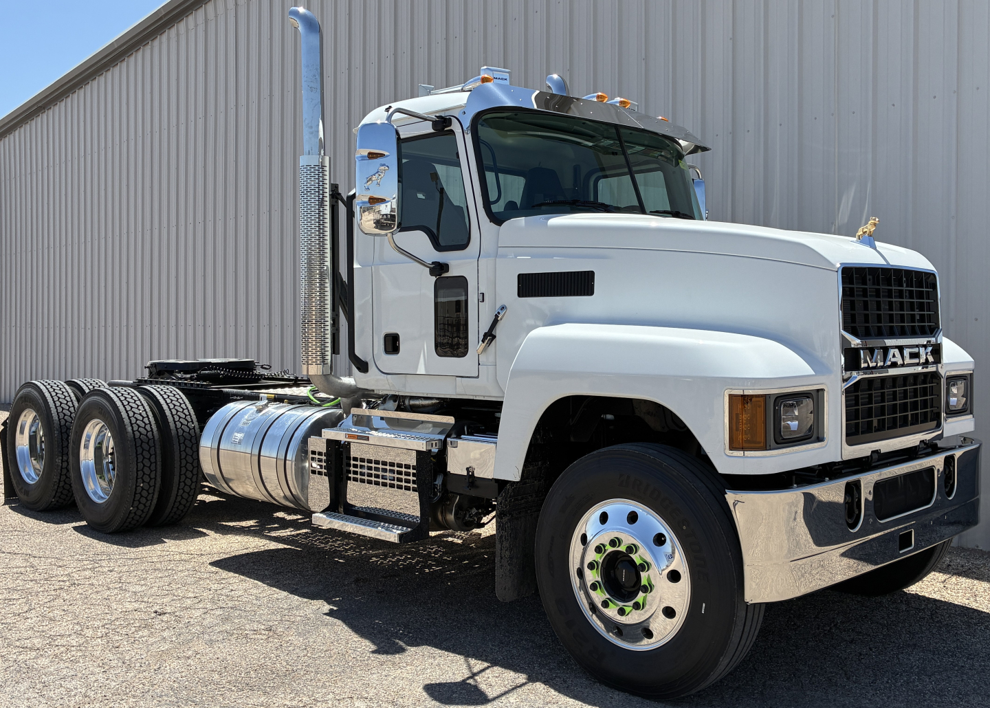 White Mack PI64T conventional daytime cab truck in profile view showing dual rear axles, chrome fuel tanks, and chrome front bumper with Mack grille.