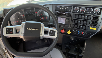 Mack PI64T truck interior showing steering wheel and dashboard with gauges and controls.
