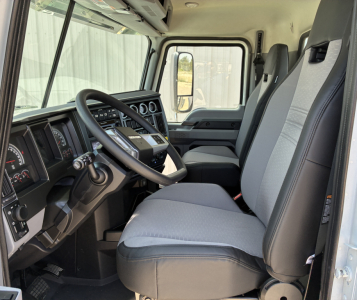 Cab interior of a 2027 Mack PI64T truck showing steering wheel, dashboard, front seats, and large side window.