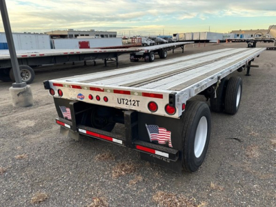 Flatbed trailer showing UT212T license plate area and dual rear axles with white wheels, aluminum deck, rear lights, and bumper with stickers.