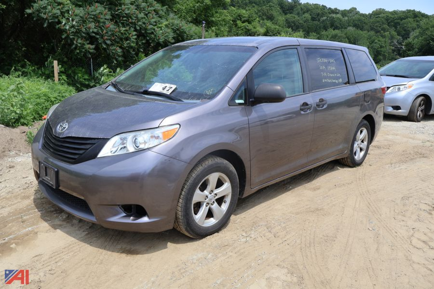 Toyota Sienna minivan in dirt lot, front-right view, windshield and side windows show handwritten listings.