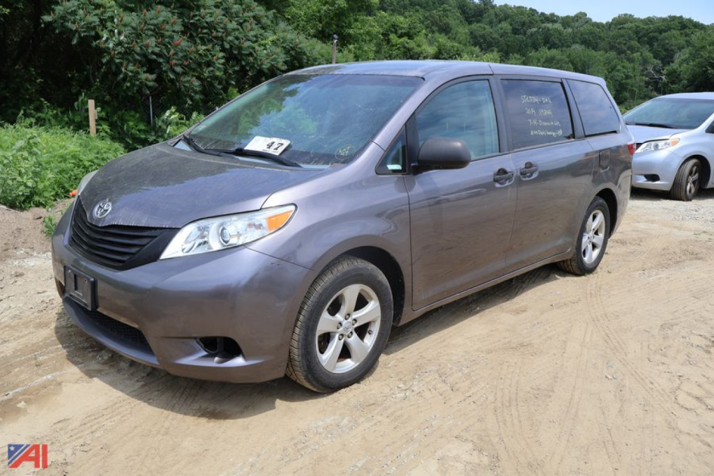 Toyota Sienna minivan in dirt lot, front-right view, windshield and side windows show handwritten listings.