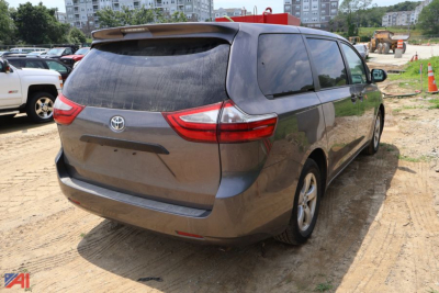 2015 Toyota Sienna minivan rear view showing Toyota emblem on tailgate, taillights, rear windshield, and riding on dirt lot.
