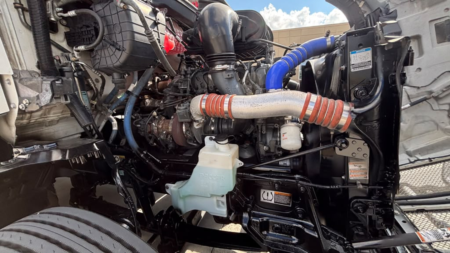 Kenworth T680 engine bay showing hoses, hoses clamps, coolant reservoir, and various mechanical components.