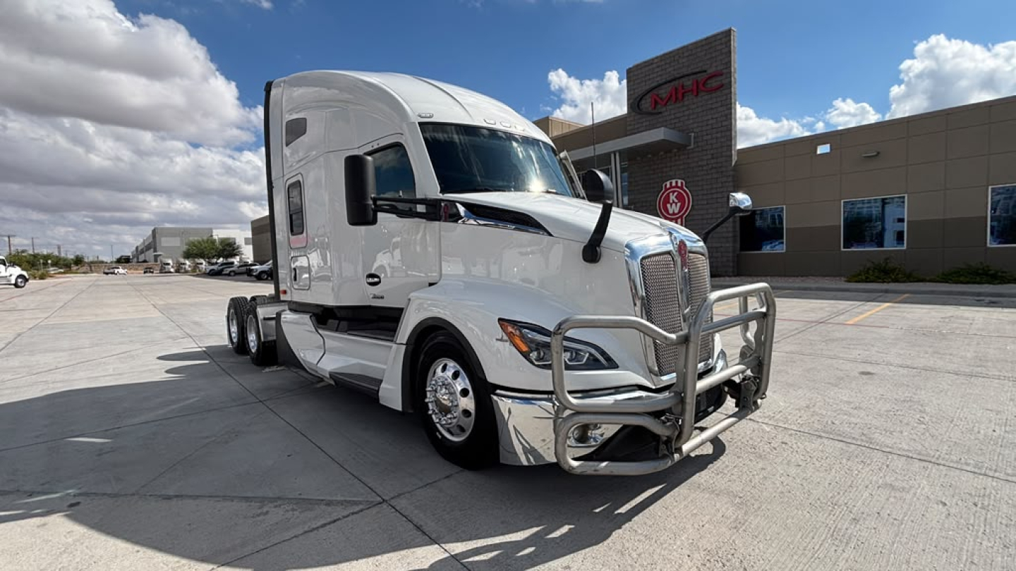 Kenworth T680 sleeper cab tractor in a dealership lot, front grille guard with chrome bumper, silver paint, VIN and stock info not visible in text