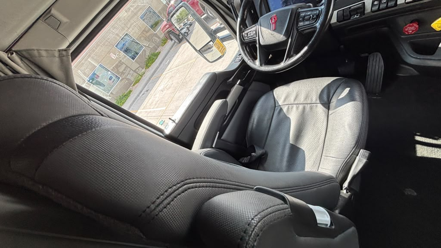 Kenworth T680 interior cab view showing steering wheel, driver seat, and dashboard area.