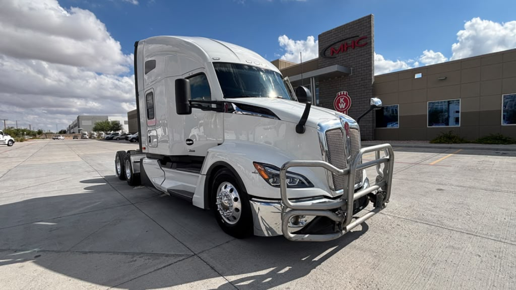 Kenworth T680 sleeper cab tractor in a dealership lot, front grille guard with chrome bumper, silver paint, VIN and stock info not visible in text