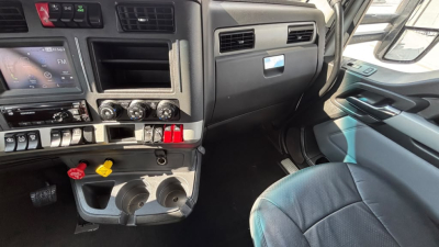 Cab interior of a Kenworth T680 showing dashboard controls, vents, and two cup holders with ignition switches and gauges visible.