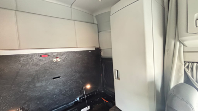 Kenworth T680 cab interior showing sleeper area with partition wall and storage cabinet, side panel, and small light in the background.