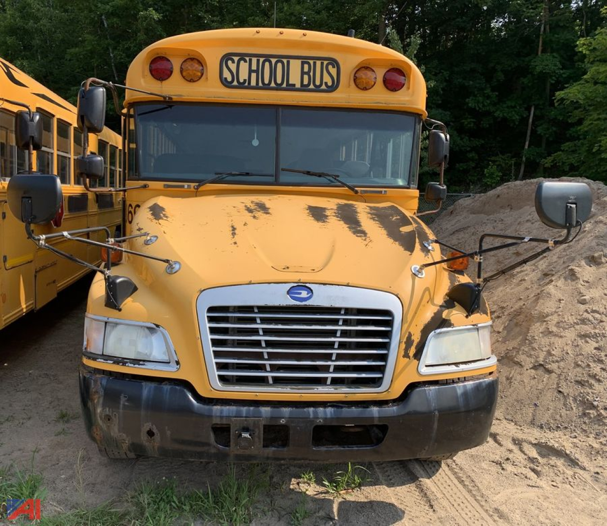 School bus front view showing yellow hardhat style hood with black paint chipping, rectangular grille, round headlamps, and a ‘SCHOOL BUS’ sign above windshield; side mirrors extend from both doors.
