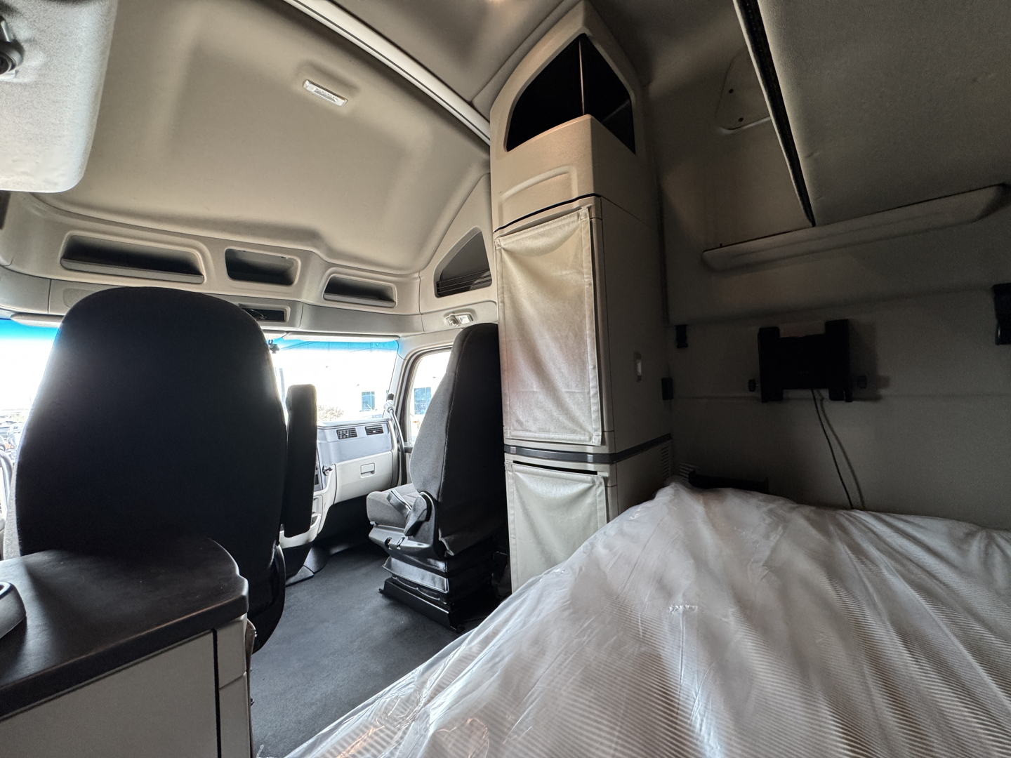 Truck cab interior of a 2023 Peterbilt 579 sleeper showing driver's seat and bunk area with overhead storage and dashboard.