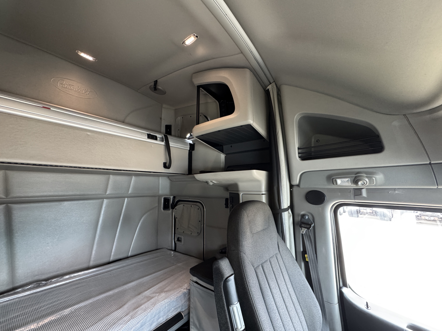 Truck cab interior showing sleeper area with overhead storage shelf and control panels; no legible text visible on components.