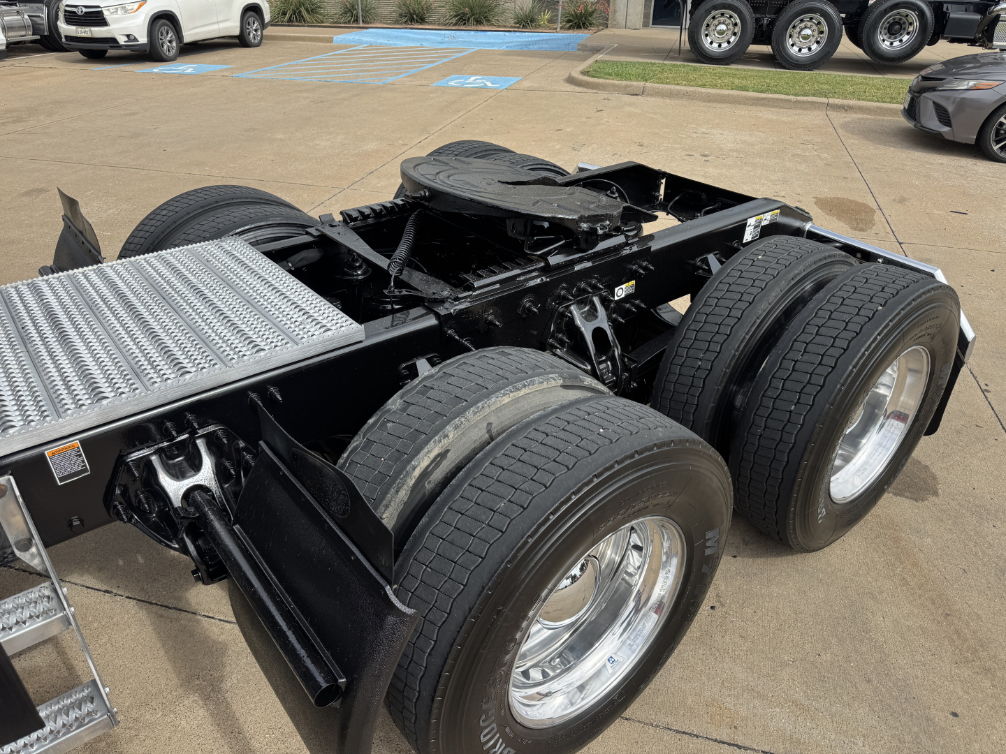 Peterbilt 579 chassis showing dual rear axles with large tires and frame, absence of cab and sleeper, aluminum fuel tank on left, dealership lot in background.