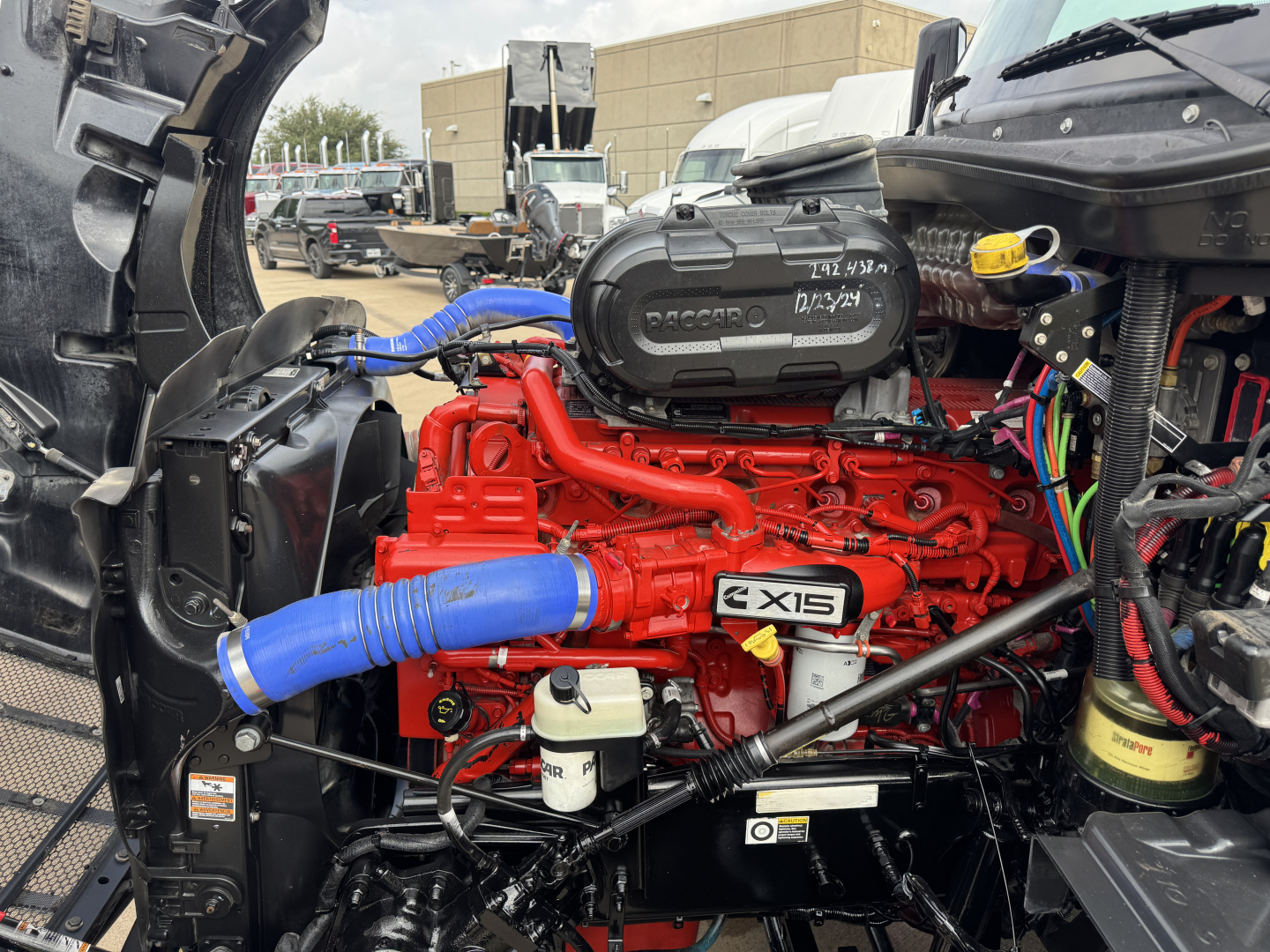 Peterbilt 579 engine bay with red engine block and blue intake hoses, visible radiator area and surrounding components.