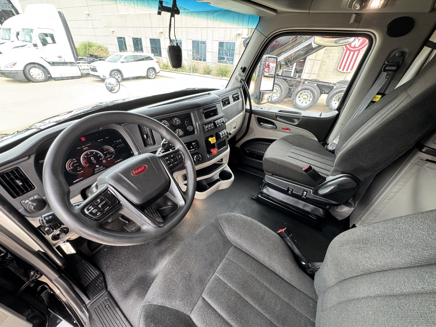 Peterbilt 579 truck interior driver seat and steering wheel with dashboard controls, gear shifter, and passenger seat in view.