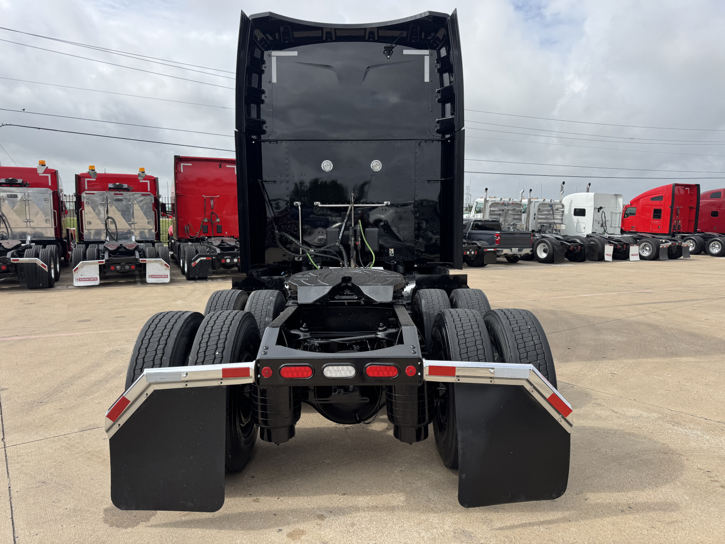 Peterbilt 579 tractor rear view shows fifth wheel area, dual rear axles, and large mud flaps; cab raised with storage area and vehicle in a truck yard.