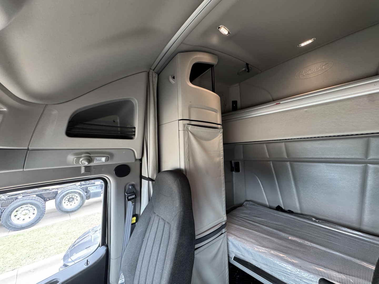 Truck sleeper cab interior of a 2023 Peterbilt 579 showing upper bunk and side storage with light gray interior panels.