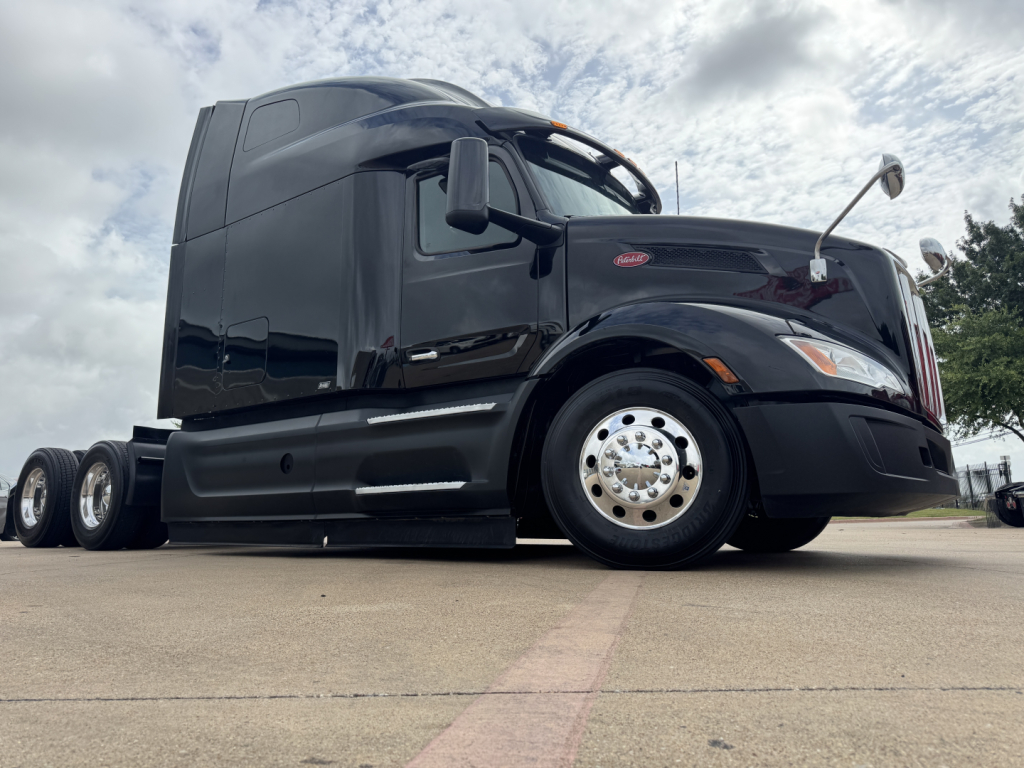 Peterbilt 579 truck side view showing sleeper cab, black paint, front fender, wheel, and chrome hubcap.