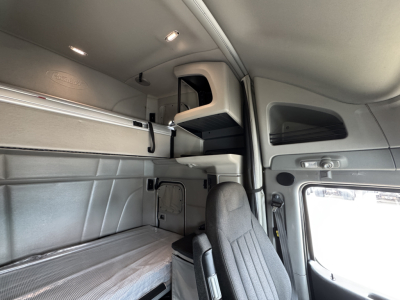 Truck cab interior showing sleeper area with overhead storage shelf and control panels; no legible text visible on components.