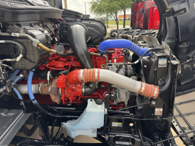 Peterbilt 579 engine bay with red engine block, blue hoses, and large intake piping visible.