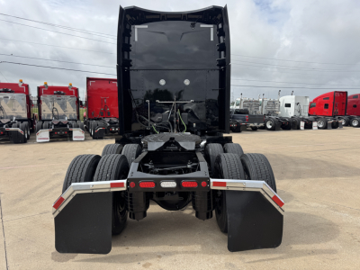 Peterbilt 579 tractor rear view shows fifth wheel area, dual rear axles, and large mud flaps; cab raised with storage area and vehicle in a truck yard.