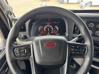 Peterbilt 579 steering wheel and dashboard view showing instrument cluster, with central Peterbilt logo on the wheel and various control stalks and gauges visible.