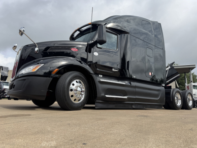 Peterbilt 579 sleepcab tractor in black, side view showing two fuel tanks, chrome wheels, and aerodynamic side skirts. Text visible on truck includes Peterbilt emblem on hood and side mirrors. 