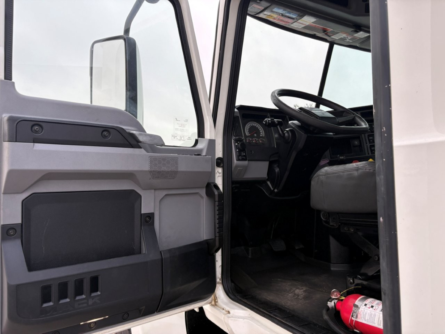 Truck cab interior view showing steering wheel, dashboard, and driver's door open in a 2020 Mack PI64T.