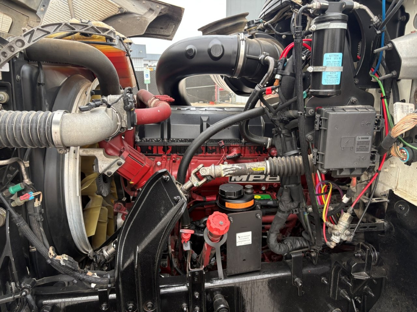 Mack PI64T truck engine bay with visible MPI turbo, hoses, wiring harnesses, and red engine components.