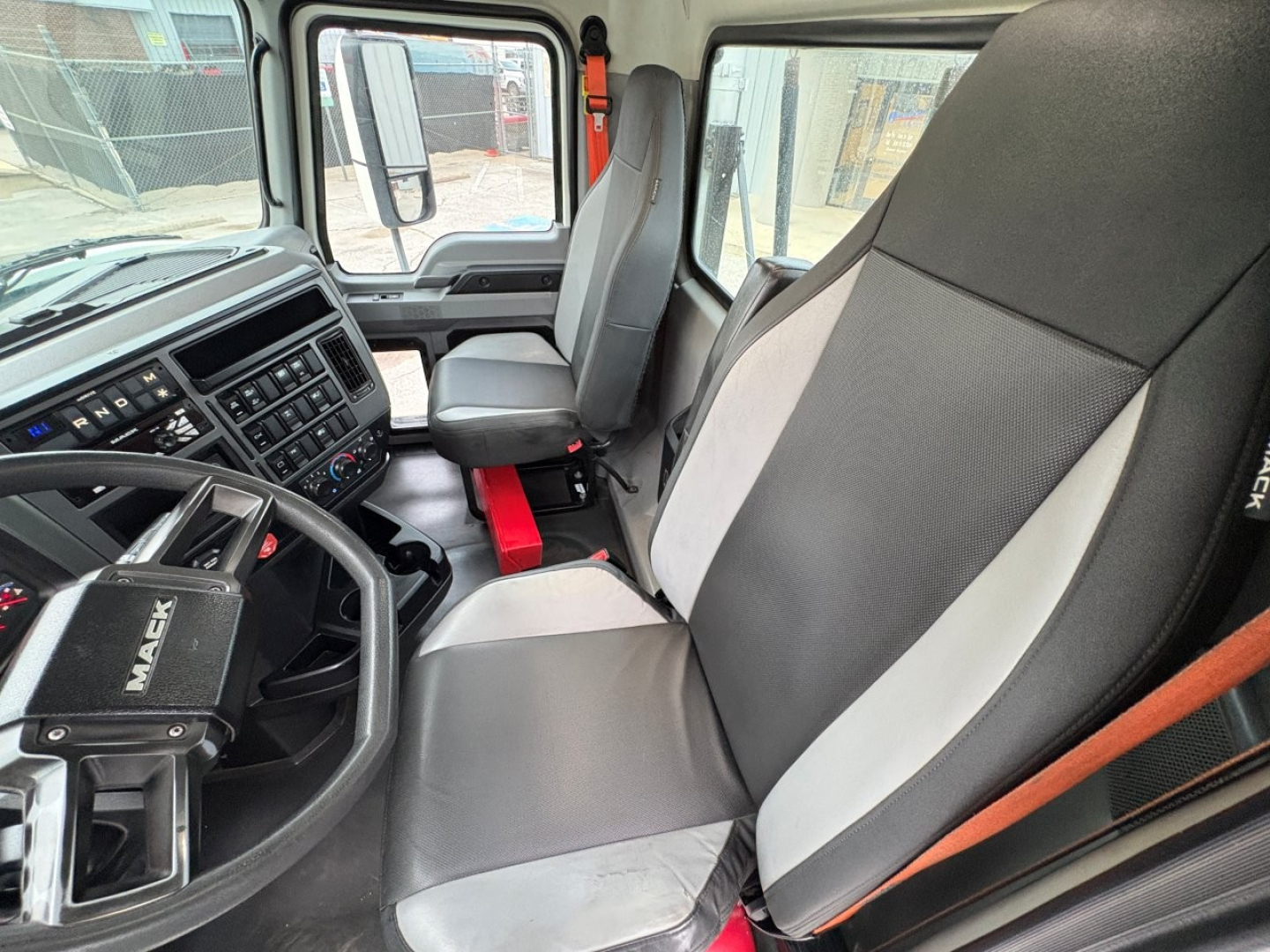 Cab interior of a 2020 Mack PI64T conventional daycab showing steering wheel, dashboard with numerous gauges, two-tone cloth seats, and center console.