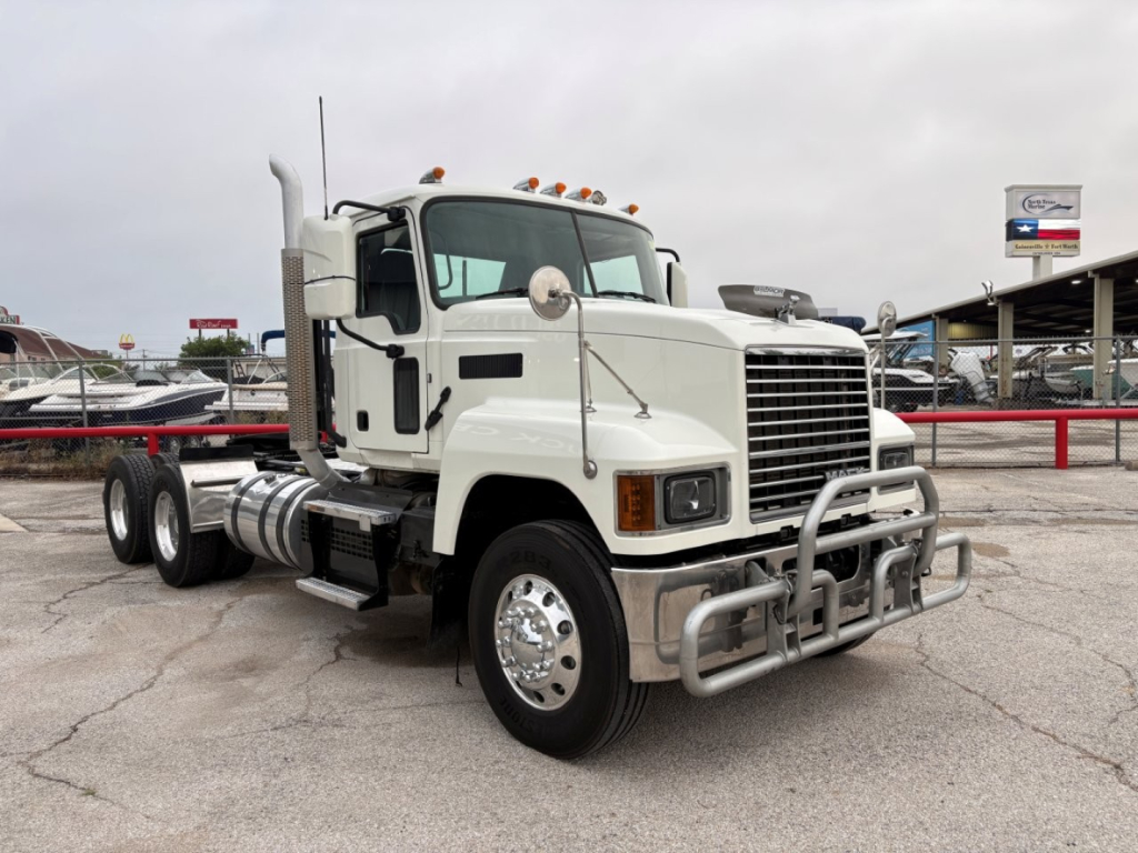 Truck cab of a white 2020 Mack PI64T conventional daycab with chrome bumper guard and dual rear axles.