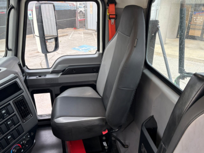 Truck cab interior with driver seat in view; gray fabric seat, black plastic dash, window, and door panel of a Mack PI64T Daycab.