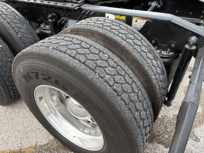 Wheel and dual rear tires of a Mack PI64T tractor showing tread, rim, and part of the chassis with a label sticker in the background.