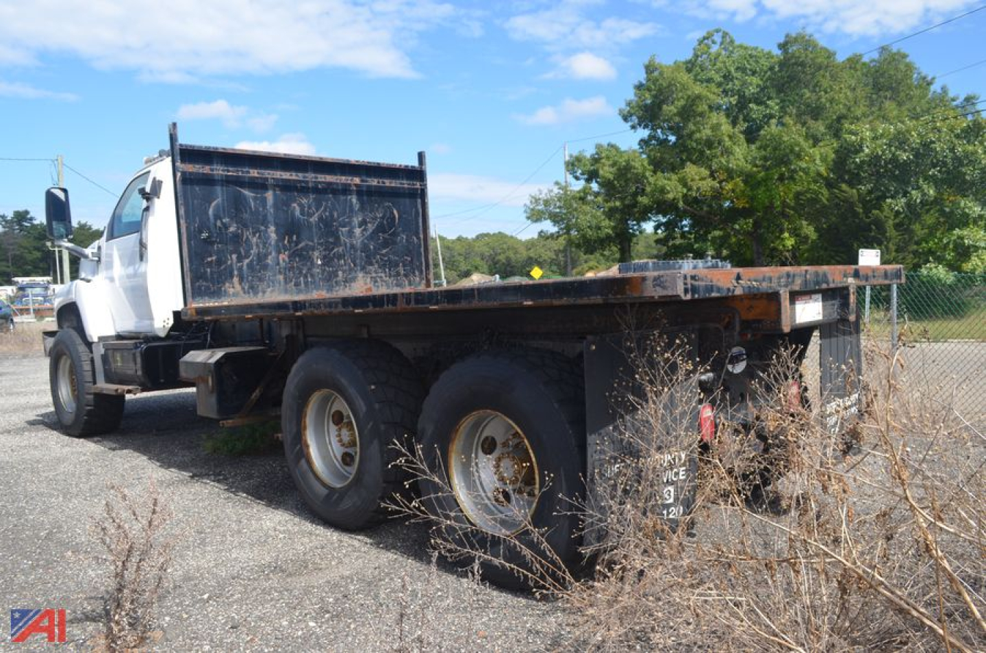 Flatbed truck shown from left-rear angle with dual rear wheels and metal flatbed.