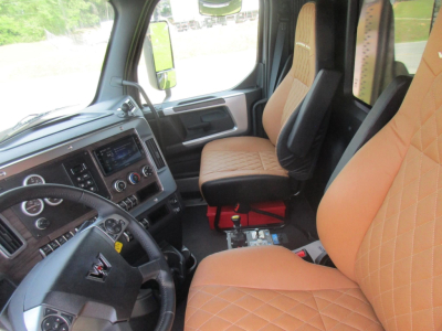 Truck cab interior showing steering wheel, dashboard, and tan diamond-stitched seats of a Western Star 49X. Front seats visible with center console and control panel.