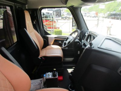 Interior of a 2026 Western Star 49X dump truck cab showing driver seat and dashboard. Visible are the steering wheel, center console, and a battery/box on the floor near the seat.