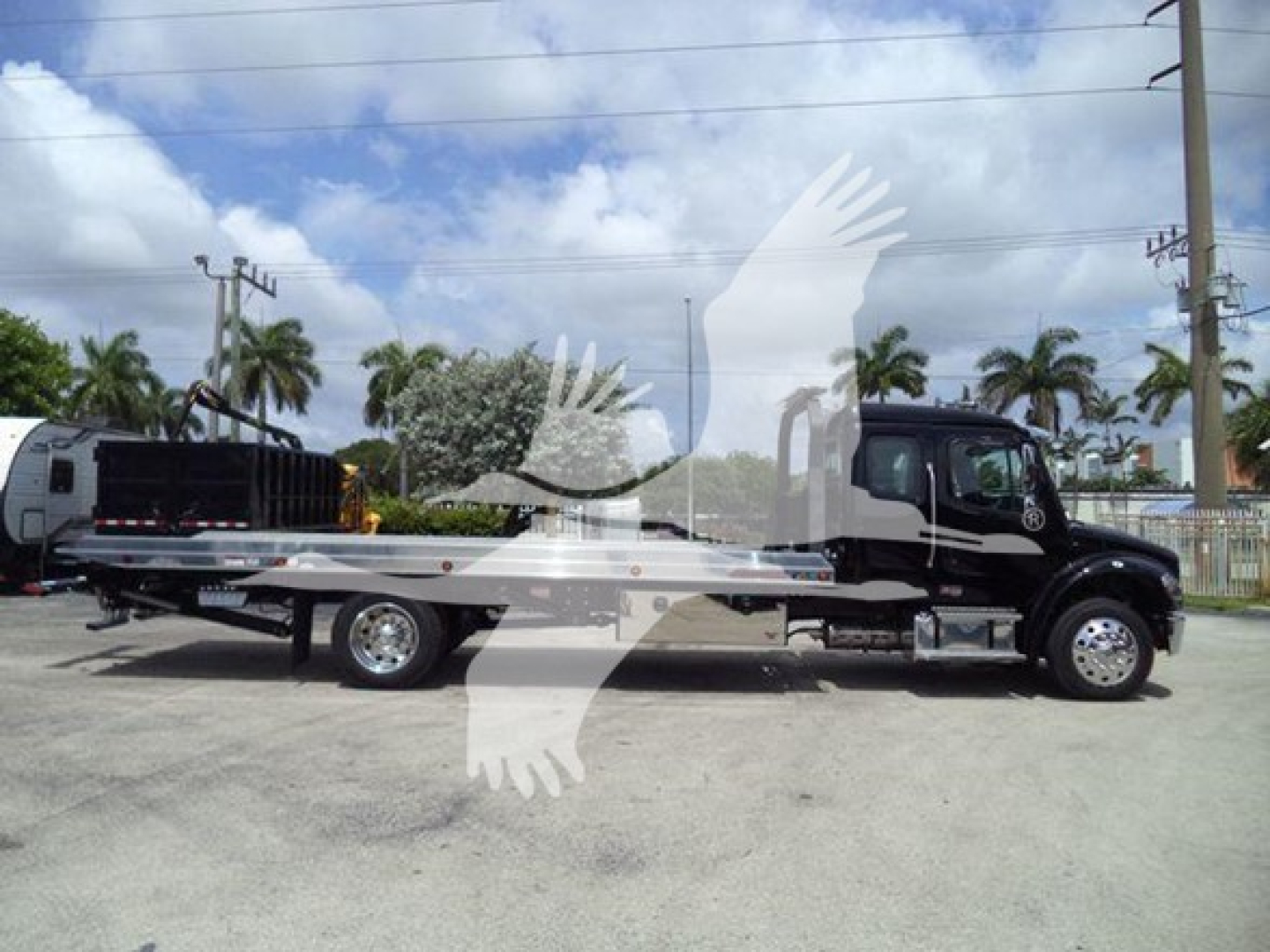 Flatbed tow truck in profile view showing Freightliner M2 106 cab and flatbed with chrome wheels.