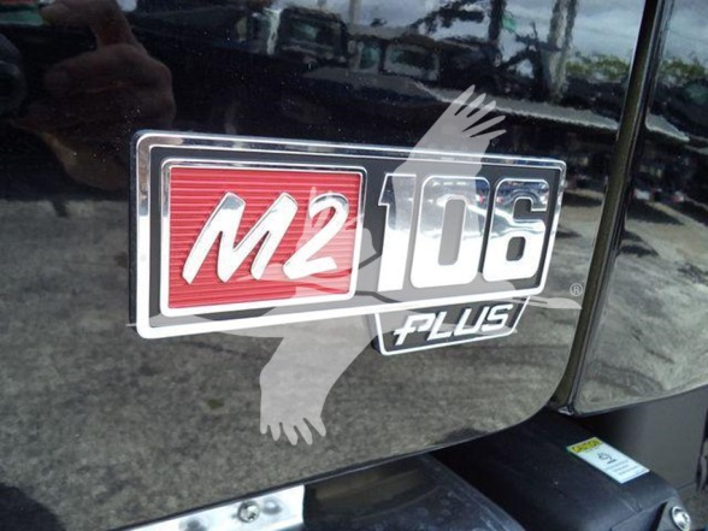 Truck badge on Freightliner M2 106 showing M2 106 Plus logo with red M2 and numeric 106 on a glossy surface.