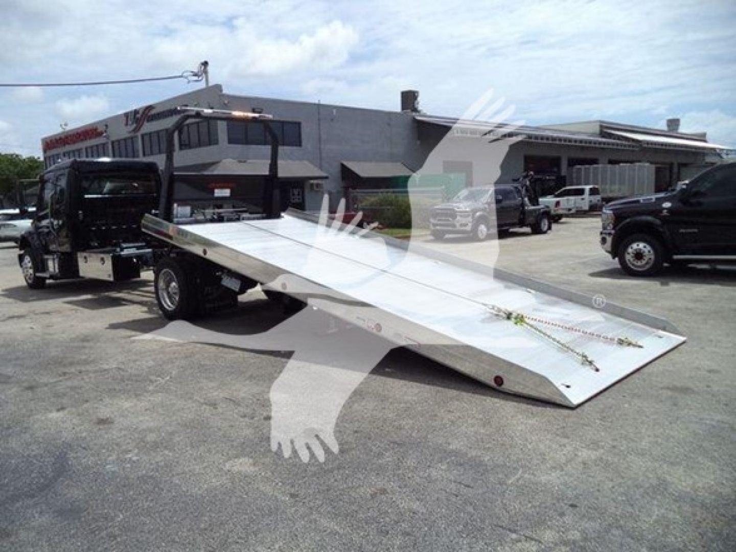 Truck rollback flatbed on a Freightliner M2 106 chassis with a long aluminum incline bed, dealership lot in background.