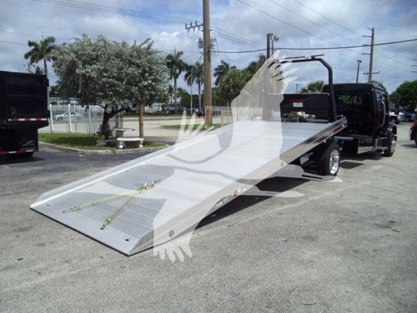 Flatbed tow truck with a silver steel ramp extending from a Freightliner M2 106 rollback truck, overall side view showing flatbed and winch area.