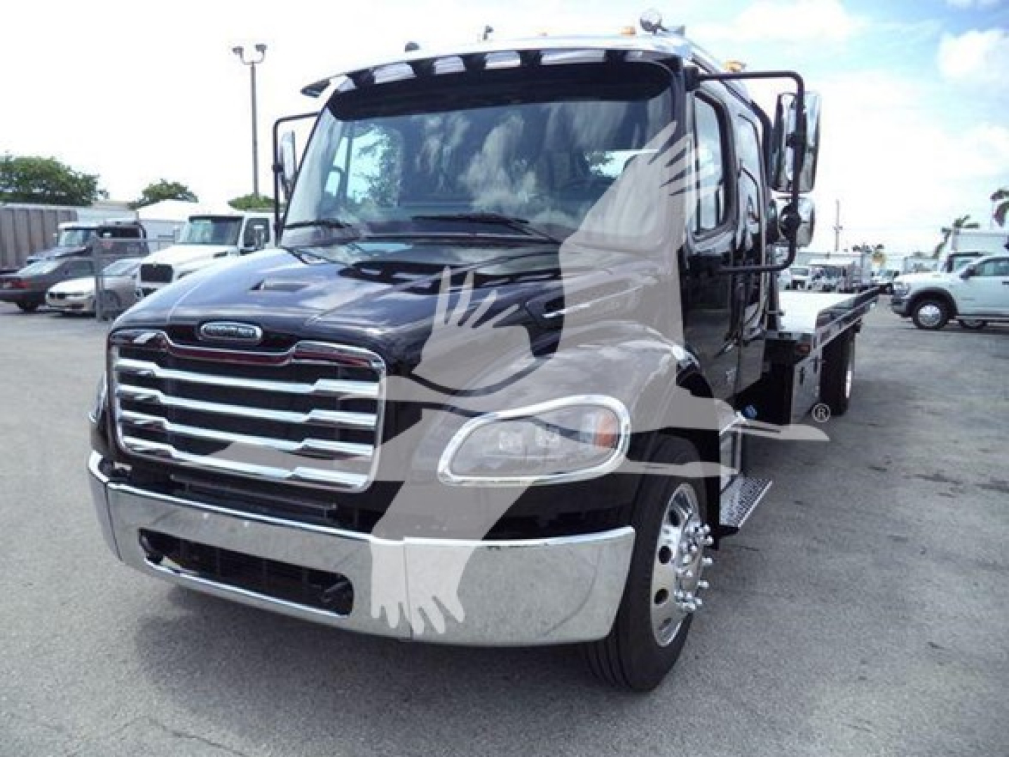 Freightliner M2 106 rollback truck shown head-on, black cab with chrome grille and side mirrors, hydraulic tow bed visible.