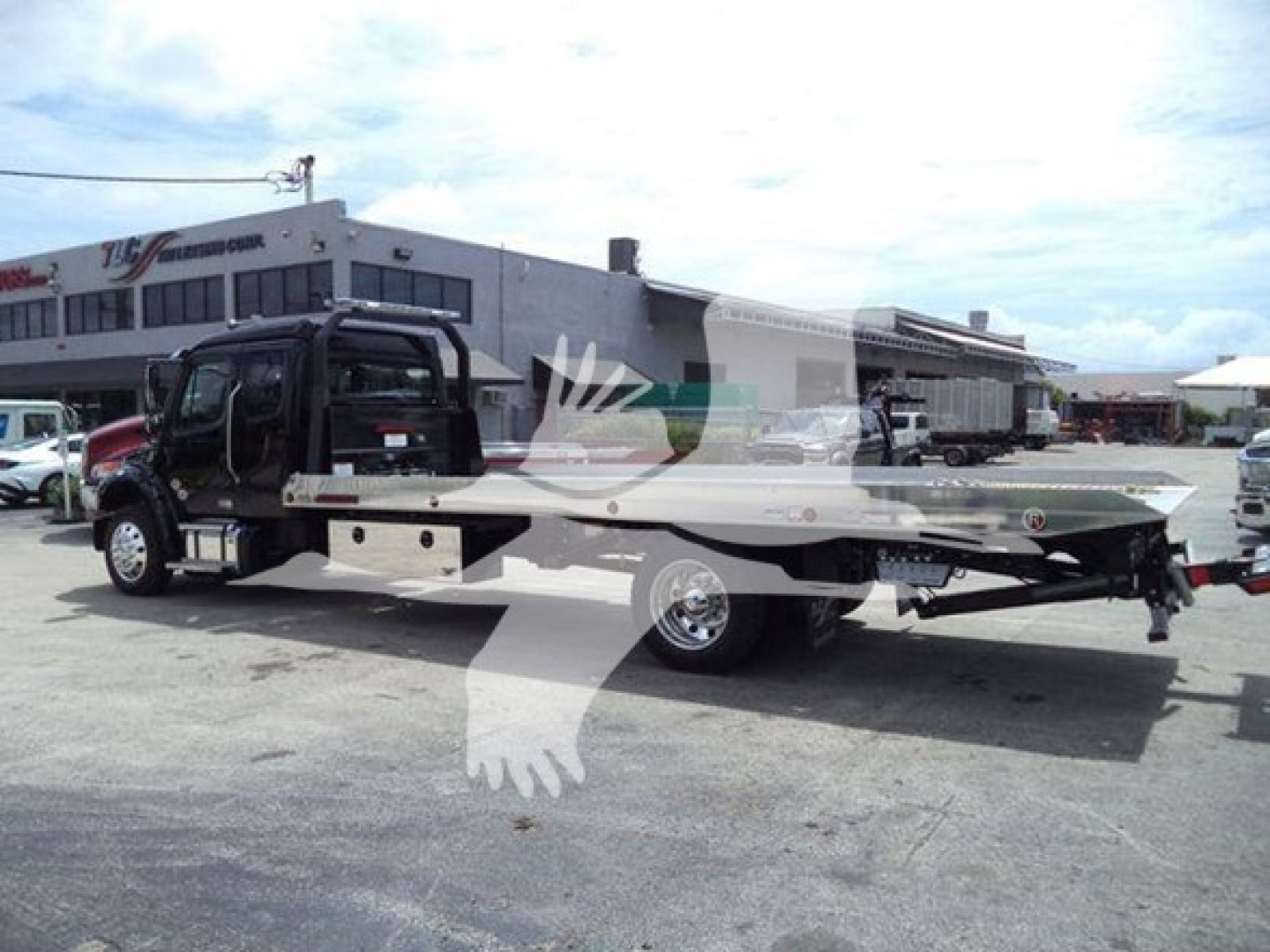 Freightliner M2 106 rollback truck in a parking lot, black cab, long flatbed with hydraulic equipment at rear.