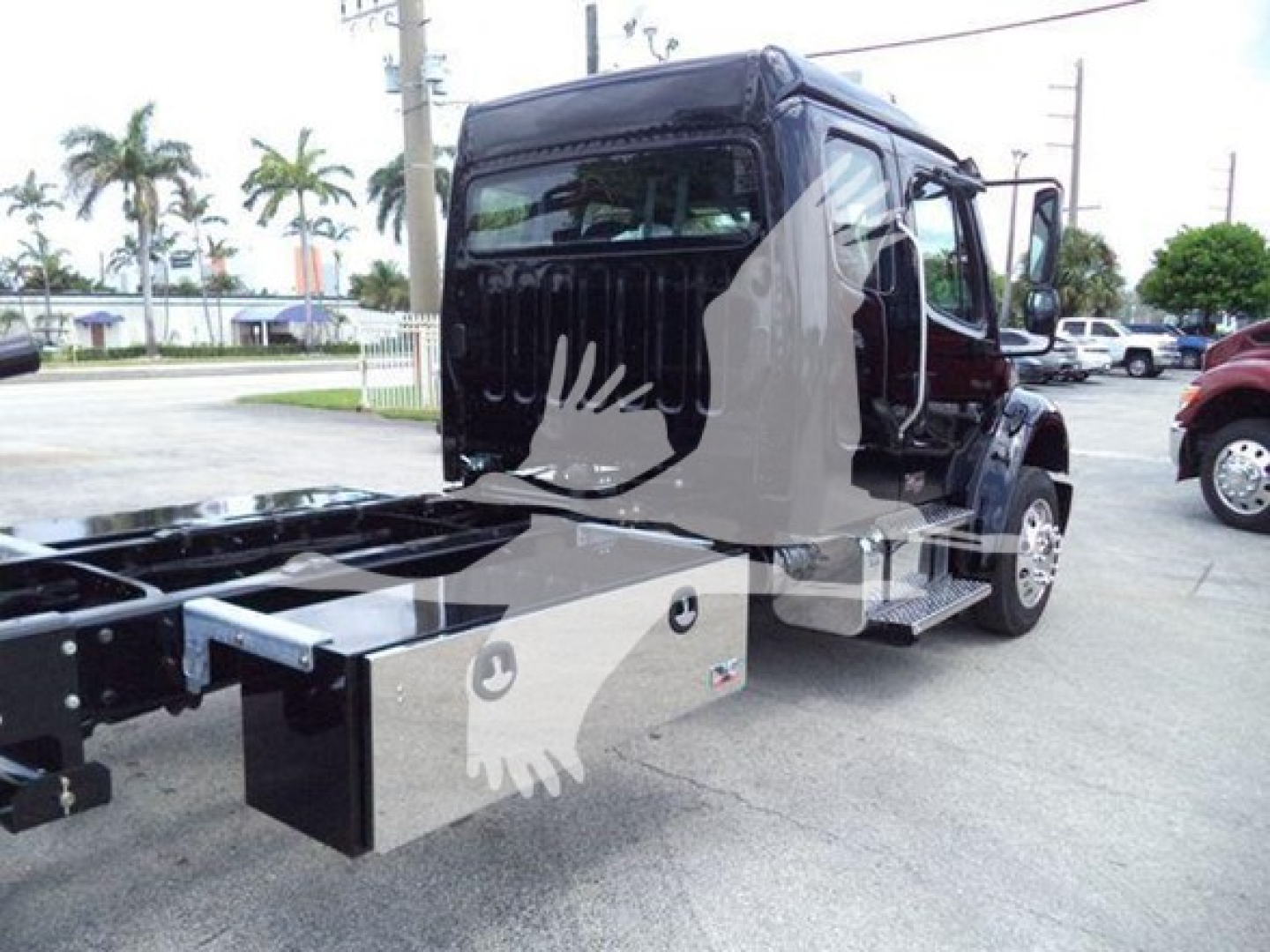 Freightliner M2 106 rollback truck seen from rear side view with flatbed chassis and operator cab, black exterior, chrome steps, and chrome toolbox visible.