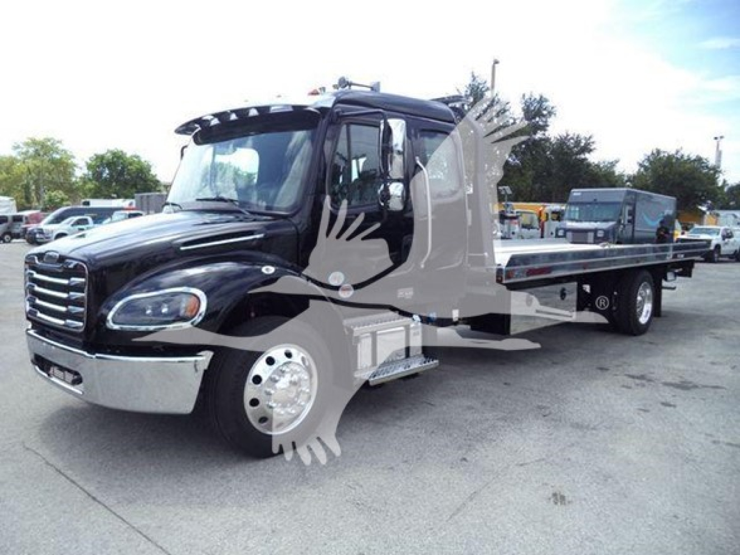 Truck cab and rollback bed showing Freightliner M2 106 with black exterior and chrome bumper, side steps, and long flatbed in a dealership lot.