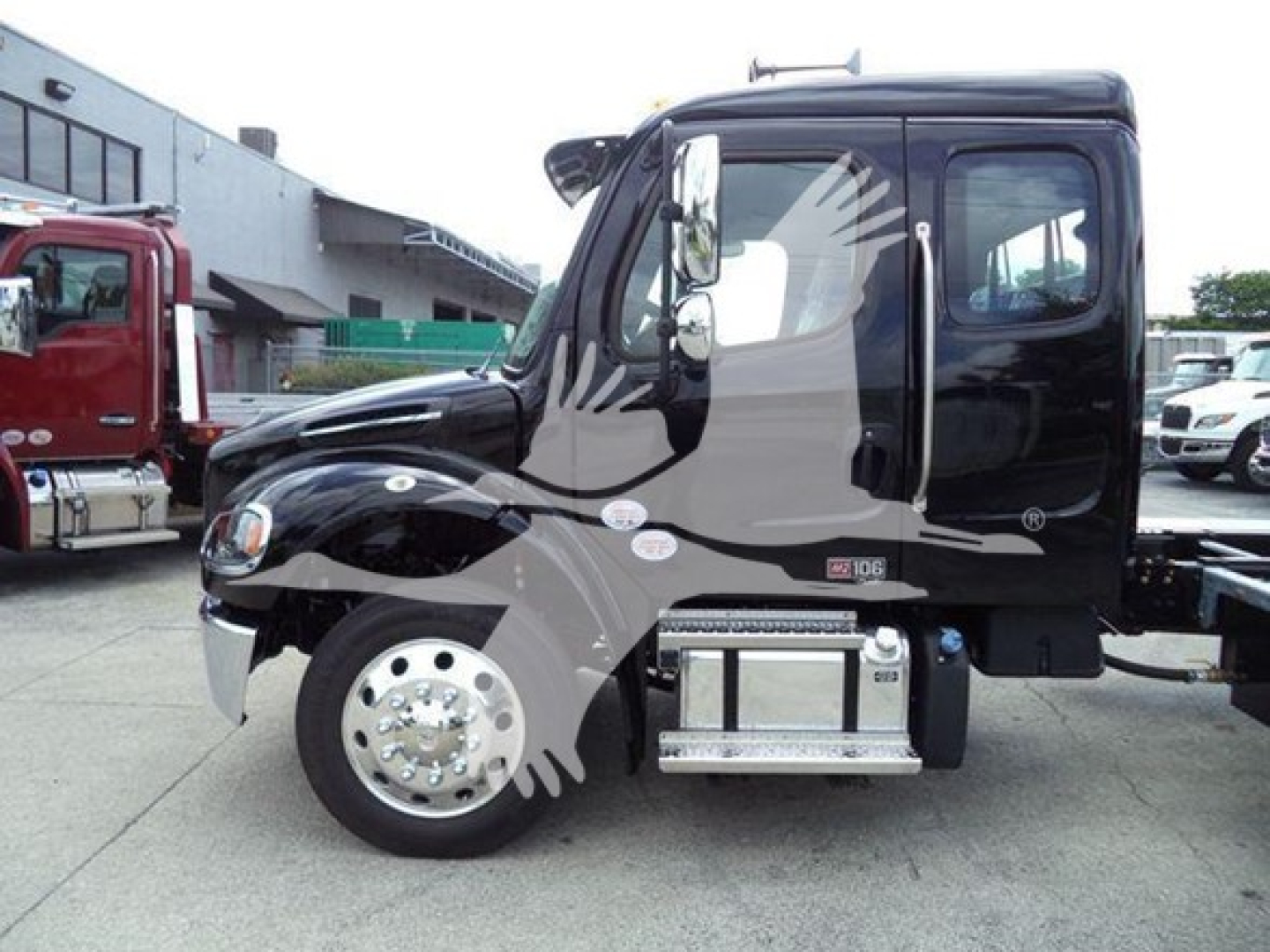 Freightliner M2 106 truck cab side view showing chrome steps and wheel, black body with decals, diesel engine bay area.