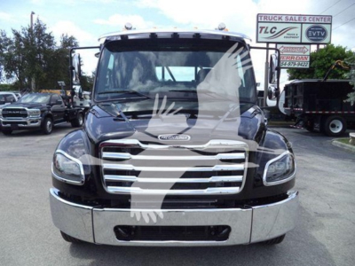 Front view of 2027 Freightliner M2 106 rollback truck showing chrome grille, headlights, bumper, and windshield with dealership signage in background.