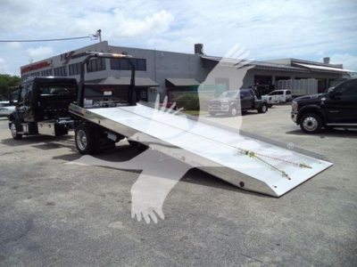 Truck rollback flatbed on a Freightliner M2 106 chassis with a long aluminum incline bed, dealership lot in background.